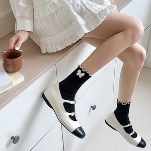 Detail of black mid-calf socks with white bows and Mary Jane shoes on a model