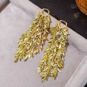 Detailed macro view of gold layered tassel earrings with leaf-shaped metal pendants