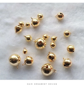 Detailed view of polished gold round bells on white plush background for DIY hair accessories