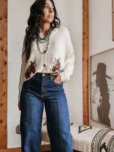 Detail van wijde jeans met hoge taille, centrale naad en wit gebreid vest met paardenprint