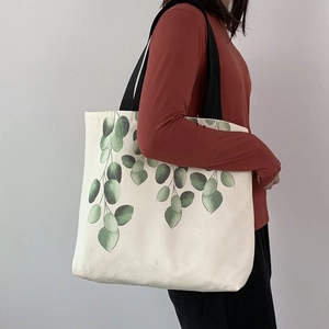 Detail of white canvas tote bag with eucalyptus print and black thick shoulder straps
