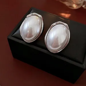 Elegant oval pearl stud earrings with silver crinkle edge on a black luxury jewelry box