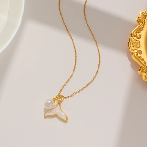Detailed view of gold fishtail pendant with white shell inlay and pearl on a fine chain