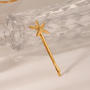 Détail d'une pince à cheveux étoile de mer dorée contre un flacon en verre sculpté