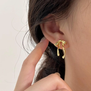 Close-up of golden bow stud earrings worn on ear showing elegant metallic texture
