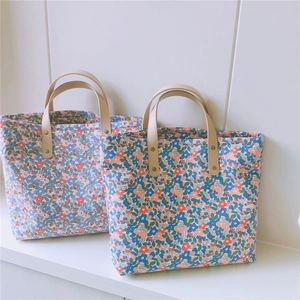 Dettaglio di due borse tote in cotone floreale con manici in pelle e rivetti in metallo