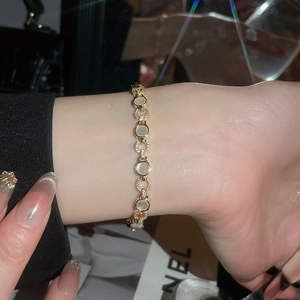 Détail d'un bracelet doré avec nacre blanche ovale et oxydes de zirconium sur le poignet