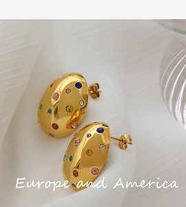 Macro detail of gold oval stud earrings with colorful zircons on white silk fabric
