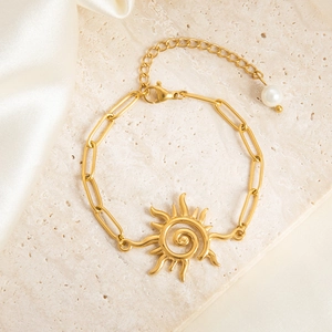 Detail of gold sun pendant bracelet with paperclip chain and a white pearl charm