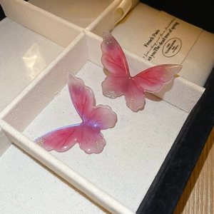 Gros plan de boucles d'oreilles papillon en résine rose pailletée dans un écrin blanc
