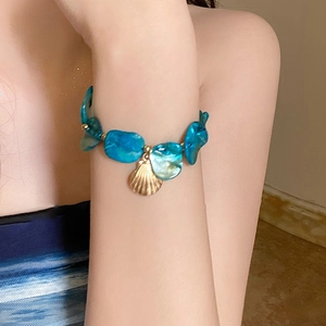 Close-up of blue shell beaded bracelet with golden fan-shaped pendant on woman wrist