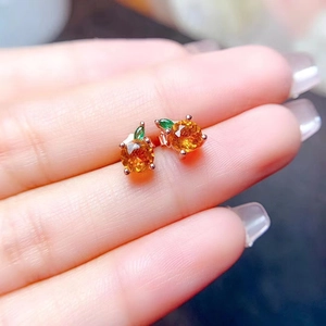 Detailed close-up of rose gold apple earrings with orange gemstones and green leaves