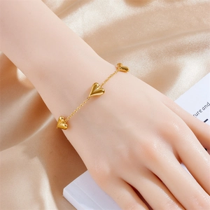 Elegant gold heart tassel bracelet in stainless steel shown on a wrist with silk background