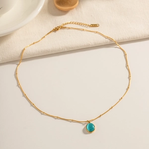 Close-up of a gold necklace featuring a blue-green oval opal pendant on beige fabric