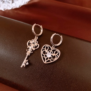 Detail of rose gold asymmetric earrings featuring a zircon heart and ornate key shape