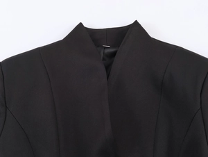 Detailed view of the stand-up collar and shoulder structure of a black pleated blazer