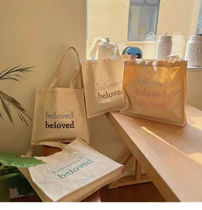 Close-up of embroidered 'beloved' letters on a cream canvas tote bag with wide straps