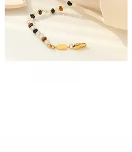 Detail of beaded bracelet with tiger eye stones and gold rectangle tag on stone surface