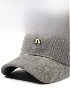 Detail of gray baseball cap featuring herringbone texture and a gold metal R logo