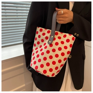 Detail of red polka dot canvas bucket bag with brown leather handles held by a model