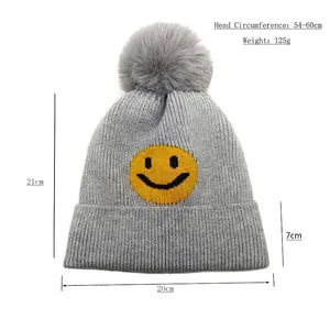 Graue Strickmütze mit Kunstpelz-Bommel und gelbem Smiley-Gesicht inklusive Abmessungen