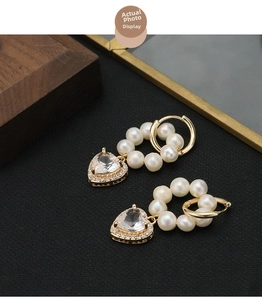Detail of heart crystal earrings with micro-pave diamonds and dangling pearls on gold hoops