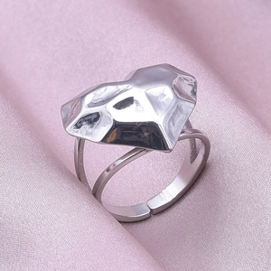 Detailed close-up of a silver geometric heart ring on soft pink silk fabric