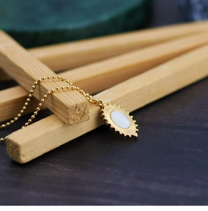 Macro detail of gold sunburst pendant with oval white shell on beaded steel chain