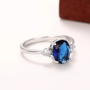 Anello elegante con tre pietre, gemma blu ovale e fascia argentata su superficie testurizzata