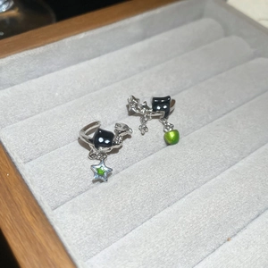 Detail of silver asymmetric star and green teardrop ear cuffs on velvet tray