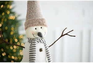 Close-up of plush Christmas snowman with knitted hat and striped scarf on festive table