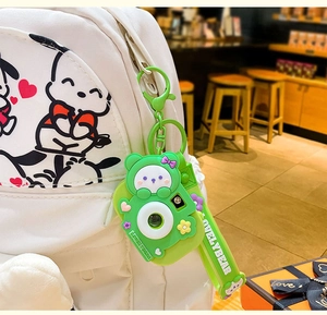 Detail of green cartoon bear camera keychain hanging on a white backpack with a green strap
