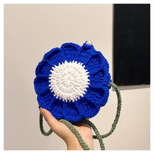 Detail of floral knit crossbody bag featuring blue petals, green strap, and pearl accent