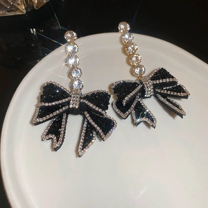 Macro shot of elegant black bow earrings with sparkling cubic zirconia border on white plate