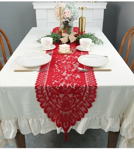 Detail of red hollow lace Christmas table runner with festive tassels and floral patterns