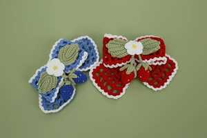 Close-up of handmade crochet hair clips featuring 3D strawberry and blueberry motifs