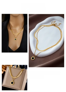 Detail of layered gold snake chain necklace with black Roman numeral pendant charm