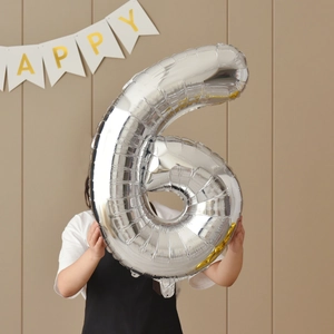 Large silver number 6 foil balloon for birthday party held by a person in celebratory scene