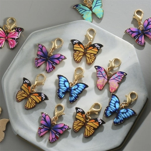 Colorful butterfly alloy pendants with gold lobster clasps displayed on a grey ceramic tray