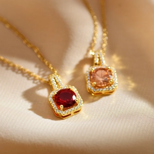 Close-up of gold square necklaces with red and champagne zircon crystals on satin