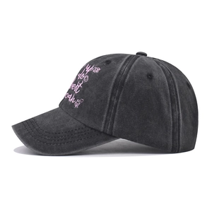 Close-up of pink floral embroidery and text on washed black denim baseball cap