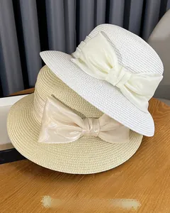 Close-up of white and beige straw sun hats with oversized satin ribbon bows on a wooden table
