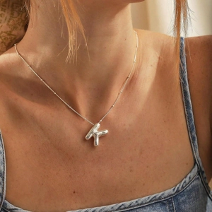 Shiny silver puffy letter K balloon pendant necklace worn by a female model