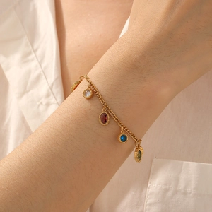 Gold chain bracelet featuring colorful geometric oval pendants worn on a woman's wrist