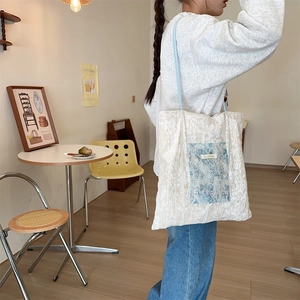 Detail of off-white lace tote bag featuring light blue floral pocket and slim shoulder straps