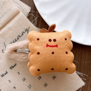 Close-up of cute yellow plush biscuit hair clip with smiling embroidery and soft fur trim