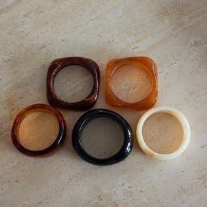 Dettaglio di cinque bracciali in resina ambra, marrone e crema su superficie di pietra