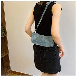 Close-up of a blue denim shoulder bag with silver metal accents worn by a model