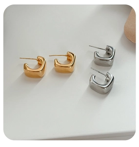 Detail of square C-shaped acrylic earrings in gold and silver polished metal finishes