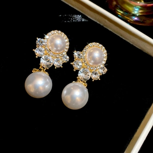 Macro shot of gold pearl earrings with crystal halo on black velvet background